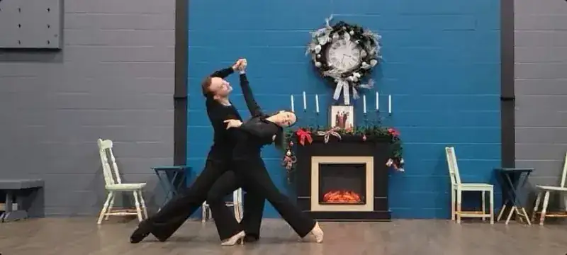 Couple in black holding a dip pose by a fireplace during ballroom dance classes at DQ Ballroom & Fitness in Ottawa