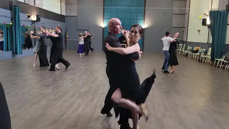 Couple in black performing a ballroom routine as the Ottawa competitive dance team practices on the floor behind them