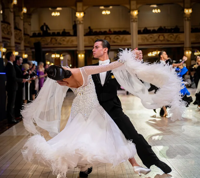 Couple in a white feathered gown and black tails dancing in a grand ballroom rentable through the DQ Ballroom & Fitness Ottawa dance studio