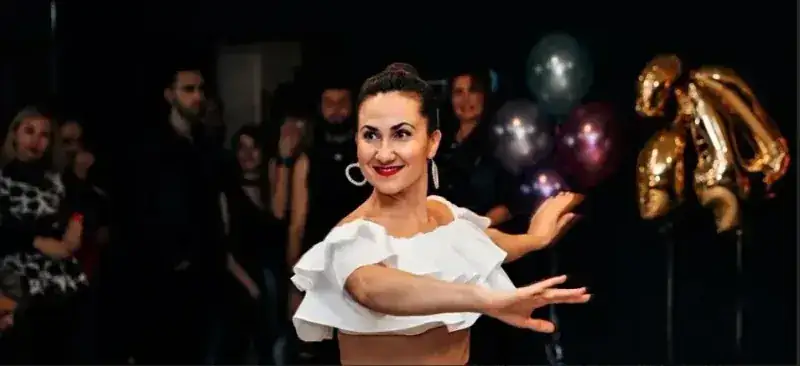 Woman in a white ruffled top mid-pose in front of an audience at a salsa and Argentine tango event in Ottawa
